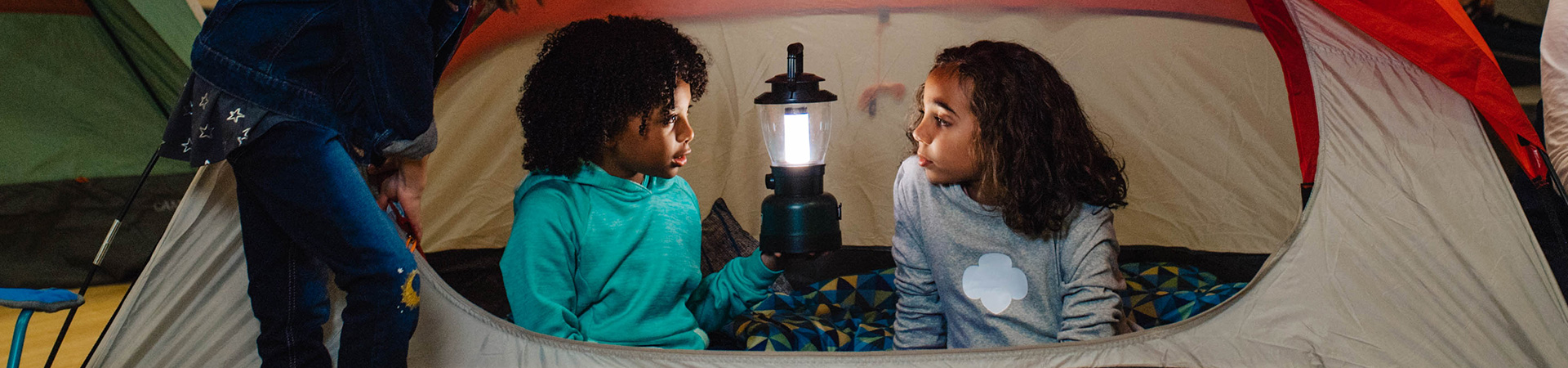  Two daisy Girl Scouts holding lantern in tent wearing trefoil shirt 
